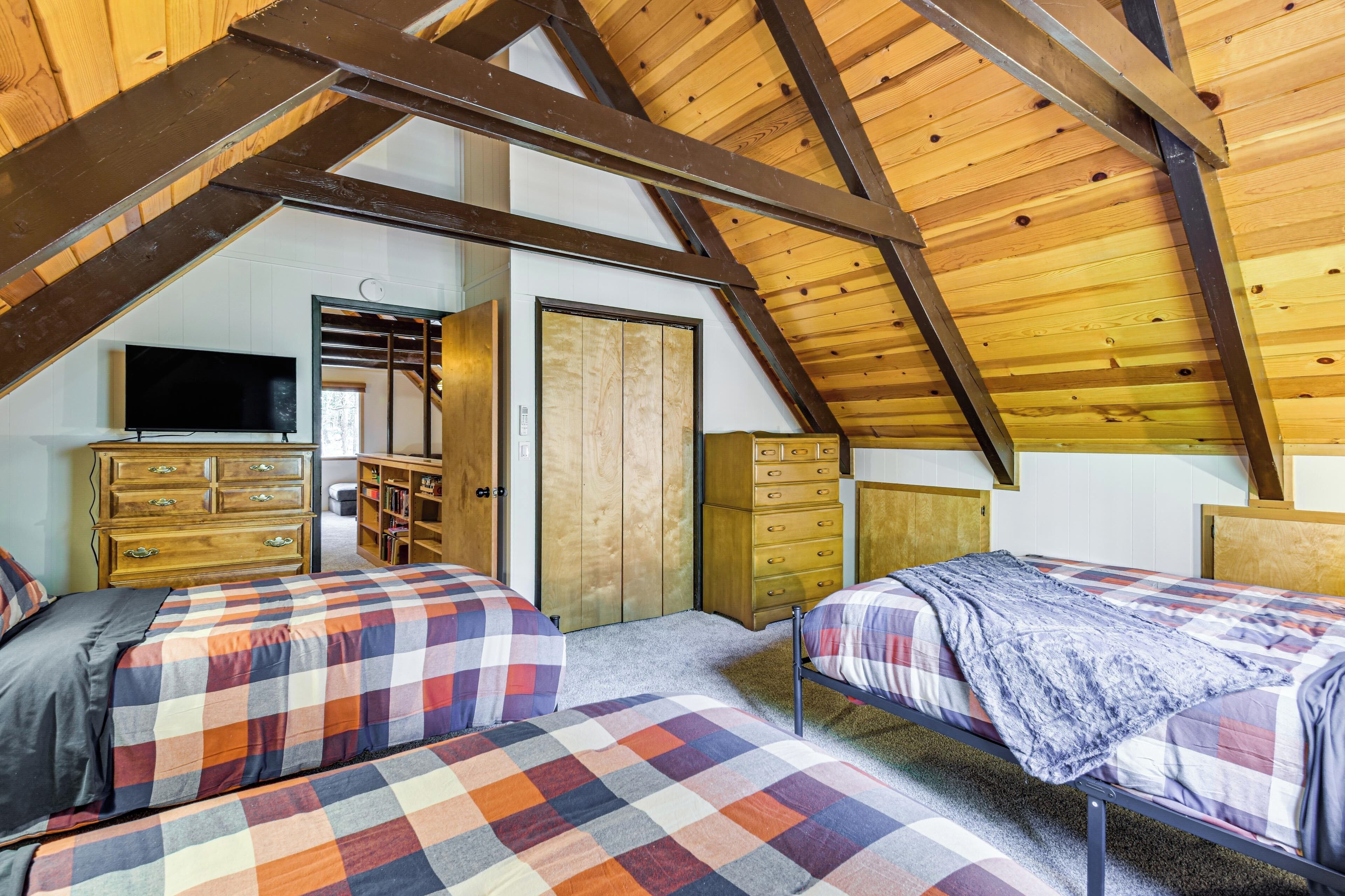An attic bedroom with two beds, wooden beams, a television, and built-in wardrobes.