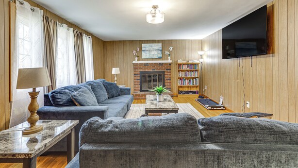 A living room with a sofa, a coffee table, a fireplace, a bookshelf, and a television mounted on the wall. - Walk to Shops & Eats! Attleboro Basecamp (Attleboro)