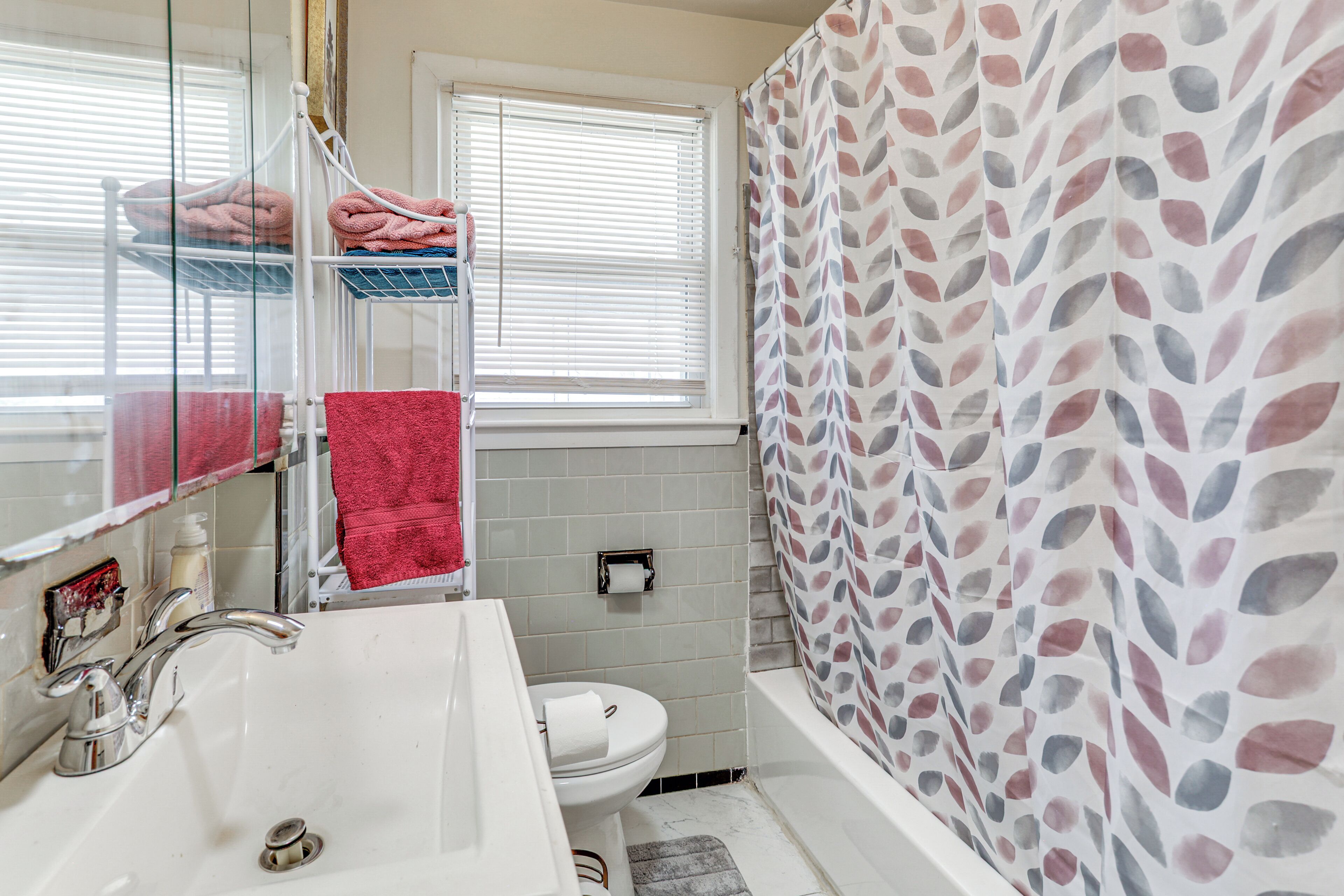A bathroom with a white sink, a toilet, a mirror, and a shower curtain with a leaf pattern.