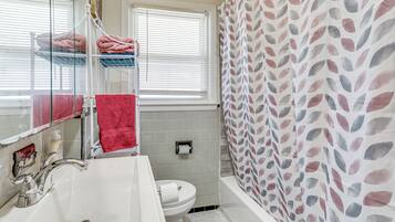 A bathroom with a white sink, a toilet, a mirror, and a shower curtain with a leaf pattern.