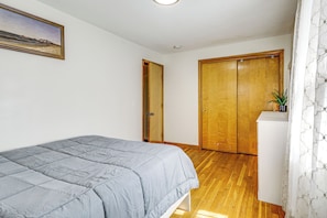 Une chambre à coucher avec un lit, une armoire en bois, une petite commode blanche et un tableau accroché au mur.