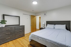 Une chambre à coucher comprenant un lit, une commode, une table de chevet, une lampe et une porte donnant sur une autre pièce.