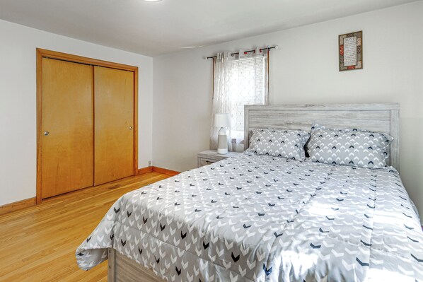 Une chambre à coucher comprenant un lit, une table de chevet, une armoire en bois et une fenêtre avec des rideaux.