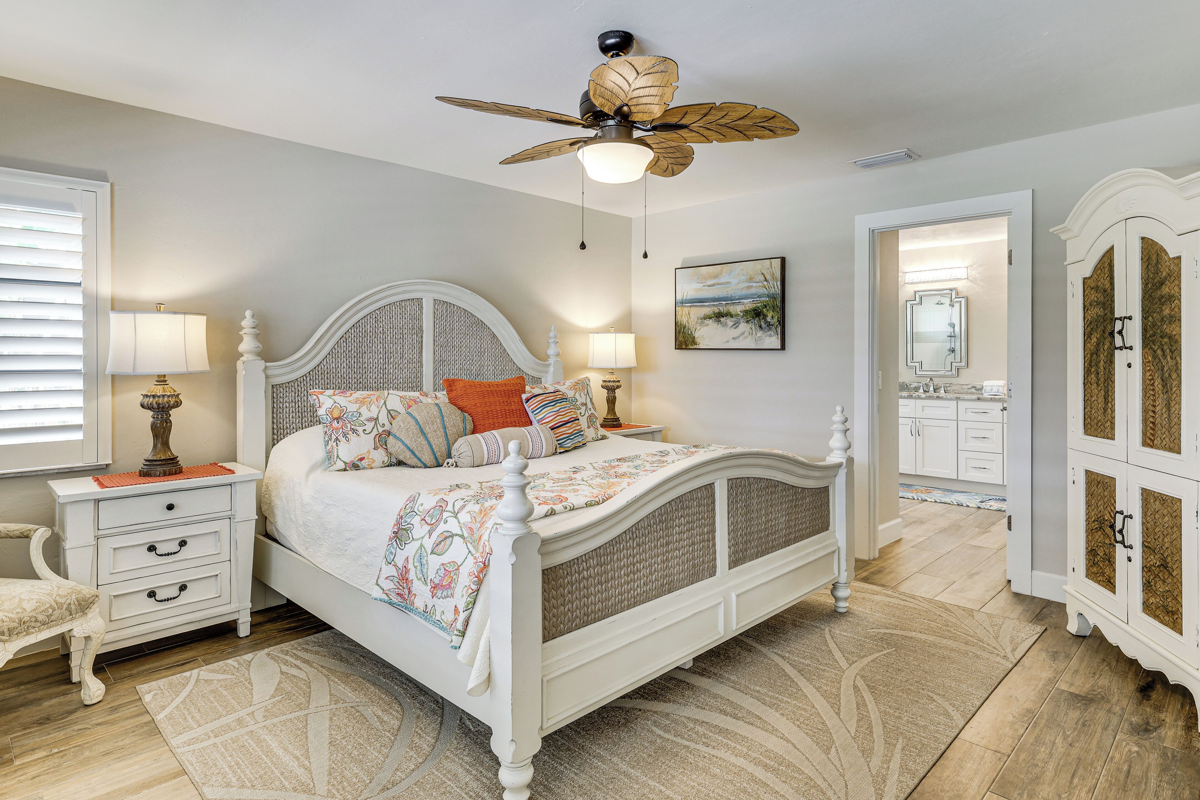A bedroom with a bed, bedside tables, a ceiling fan, and a view into the bathroom.