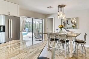 Eine moderne Küche mit Marmorarbeitsplatte, Edelstahlgeräten und einem Essbereich mit Glastisch und Metallstühlen.