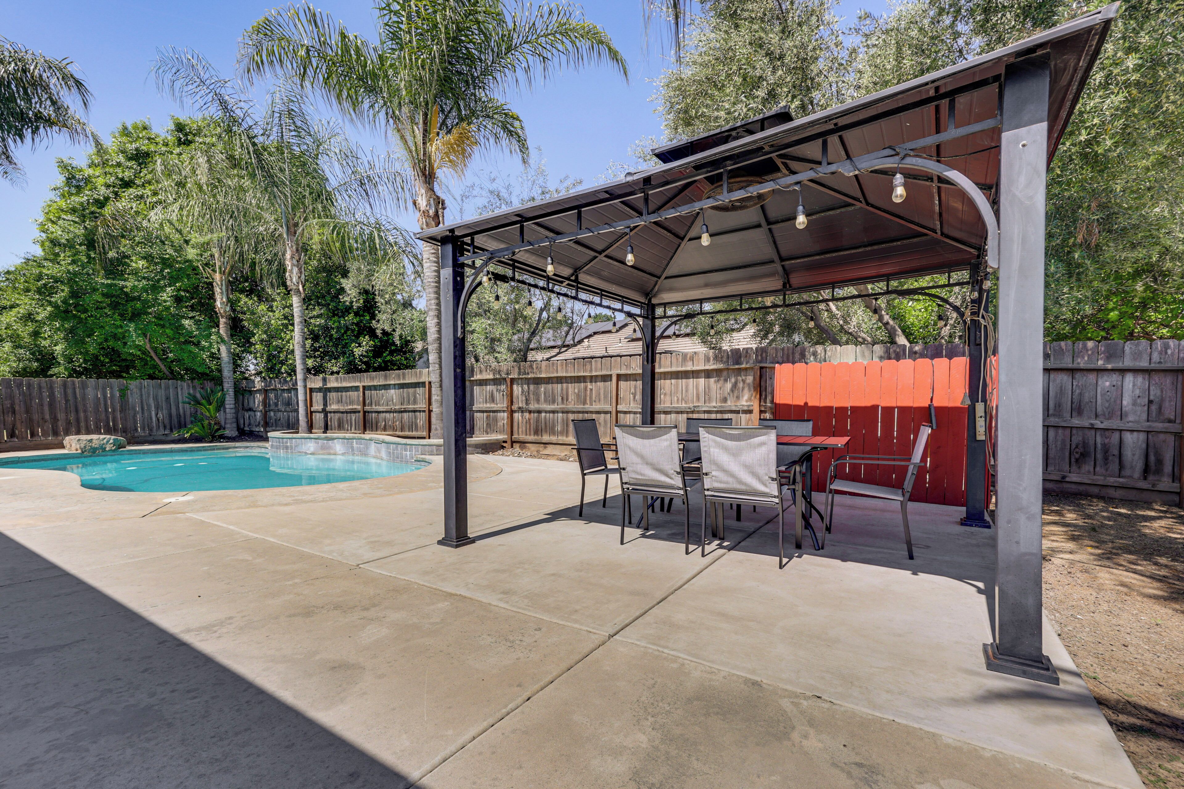 A covered patio area with a pool, outdoor furniture, and a wooden fence.
