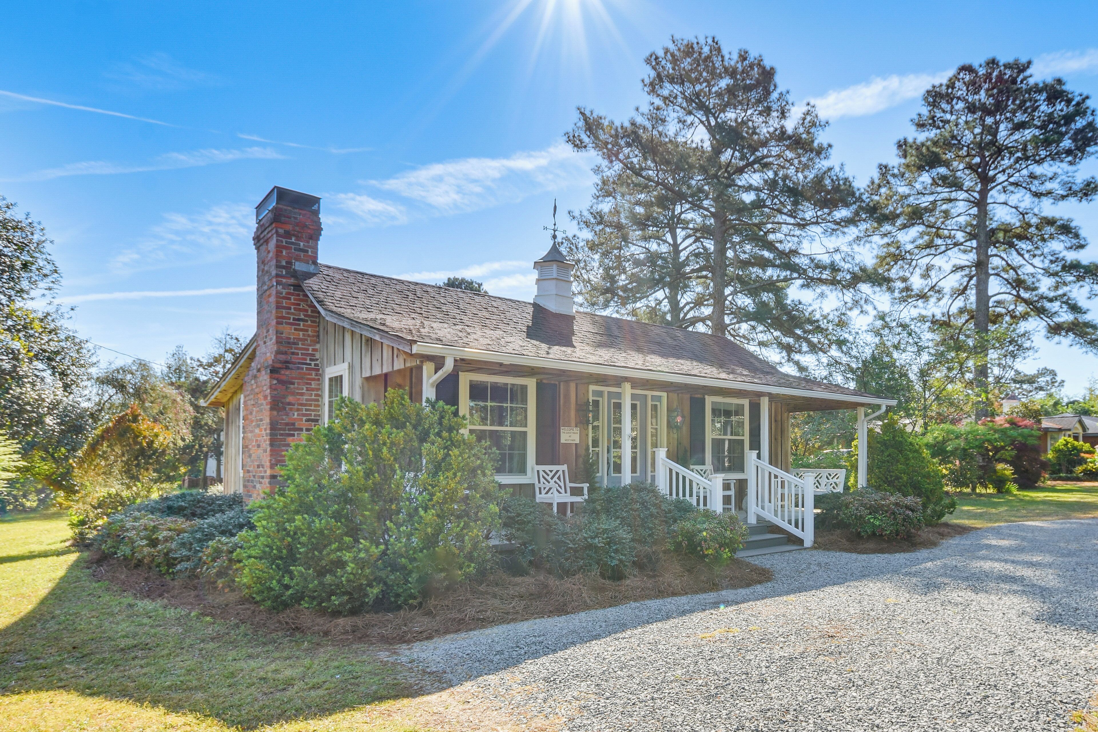 A single-story house with a brick chimney, a porch with white railings, and a gravel driveway.