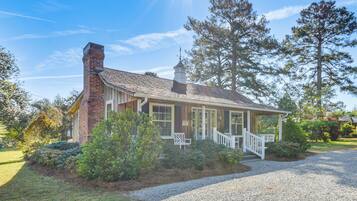A single-story house with a brick chimney, a porch with white railings, and a gravel driveway.