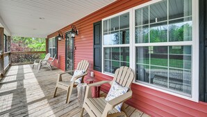A covered porch with Adirondack chairs, a wooden deck, and large windows overlooking a green landscape. - 3 Mi to Nolin Lake Boat Ramp! Family Home w/ Deck (Mammoth Cave)