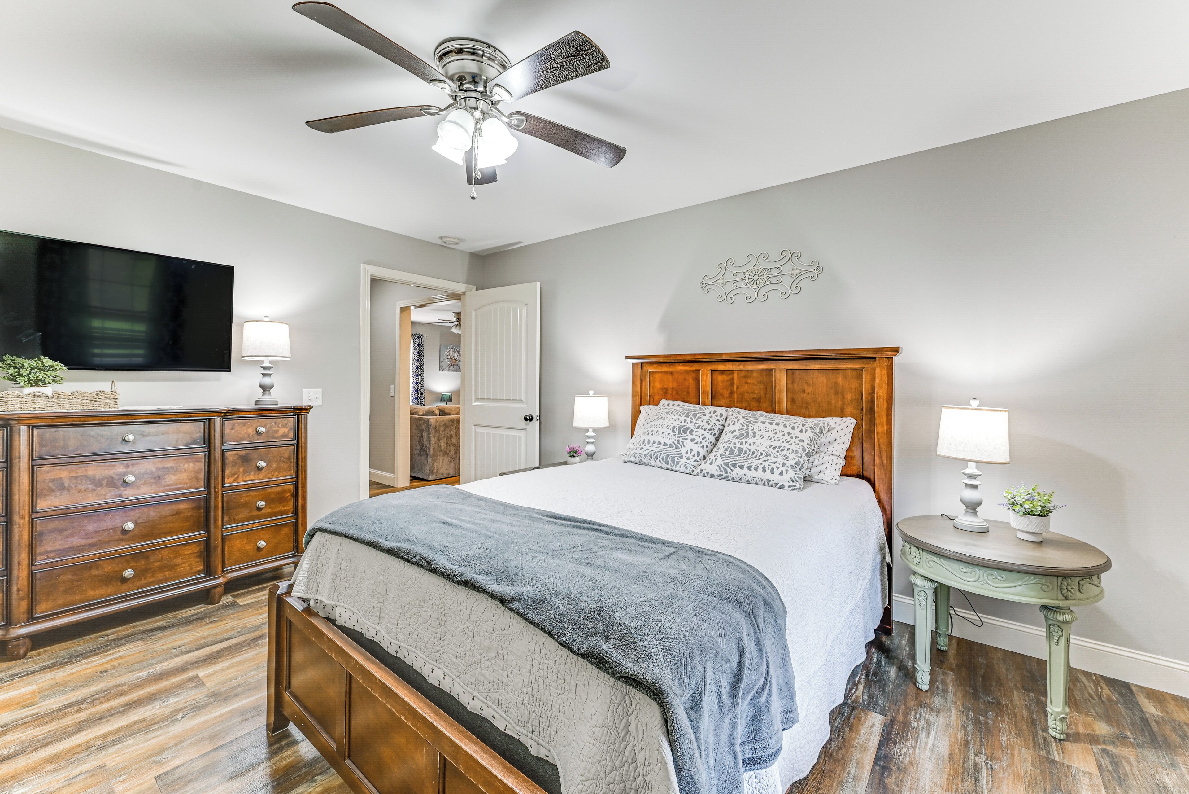Une chambre à coucher comprenant un lit, une commode, une coiffeuse et un ventilateur de plafond.