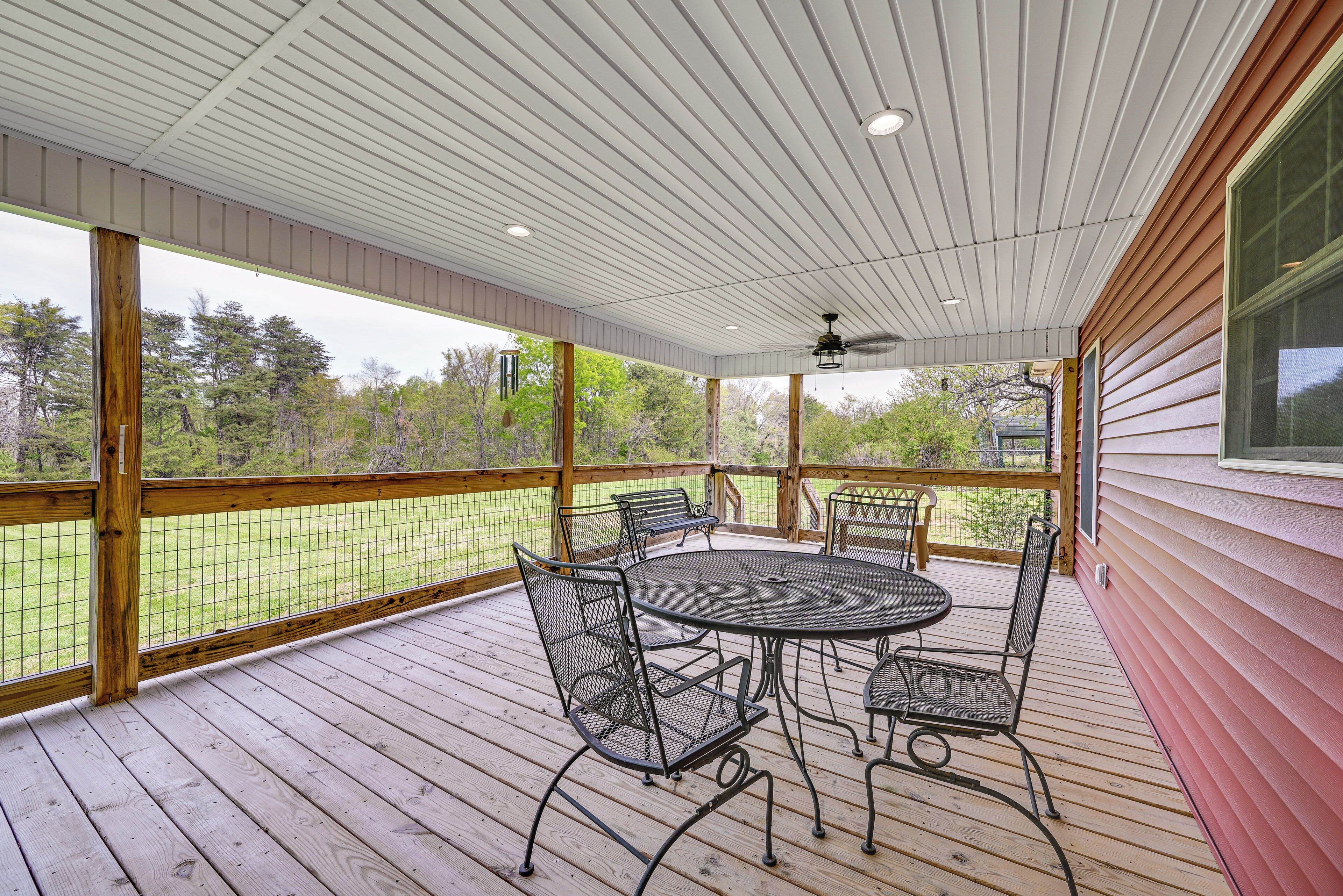 A covered patio with a round table and chairs, a ceiling fan, and a view of a grassy area.