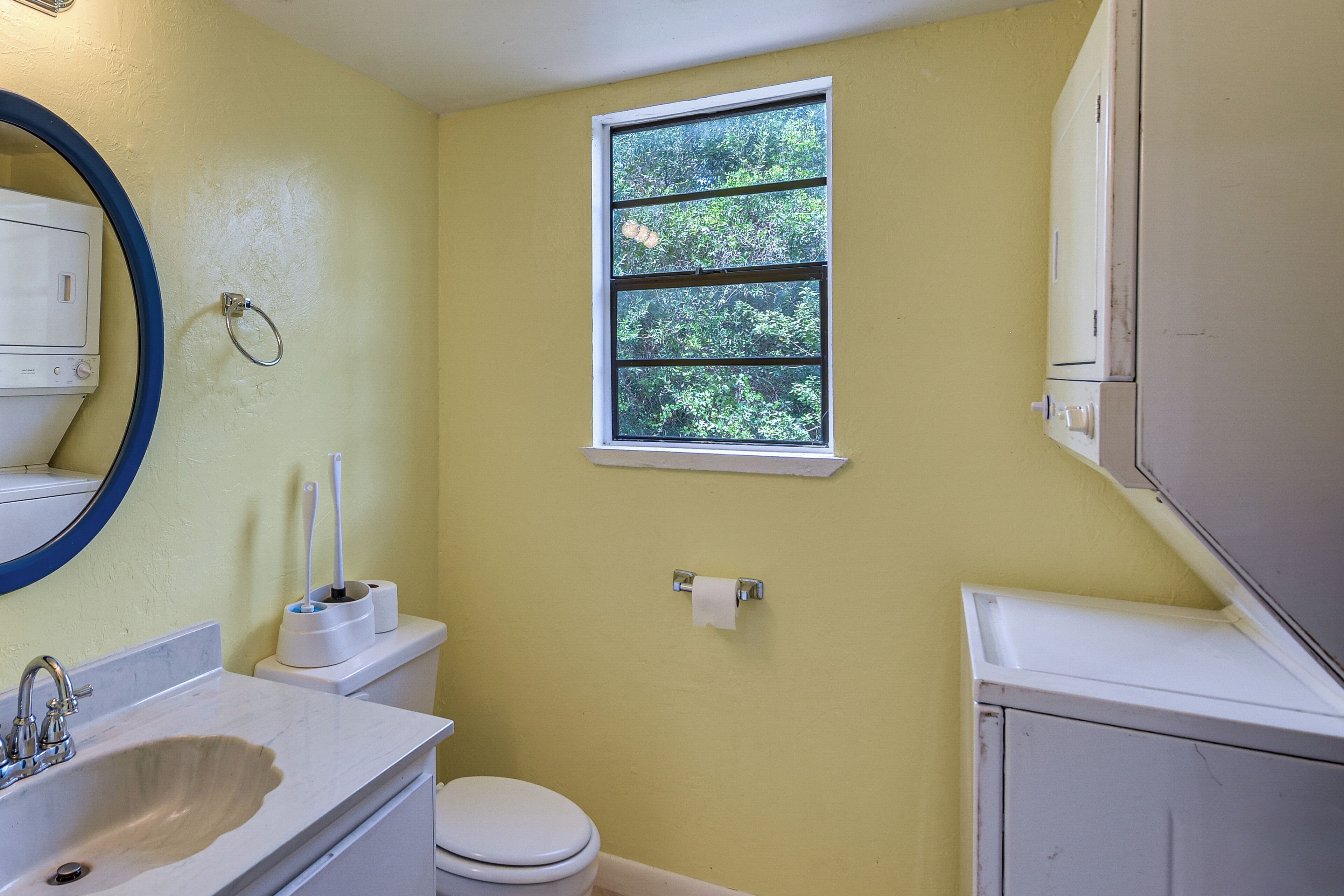 Un baño con inodoro, lavabo, espejo, ventana y toallero.