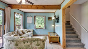 Ein Zimmer mit einer gebogenen Couch, einem Deckenventilator, einer Treppe und einem Fenster mit Aussicht.