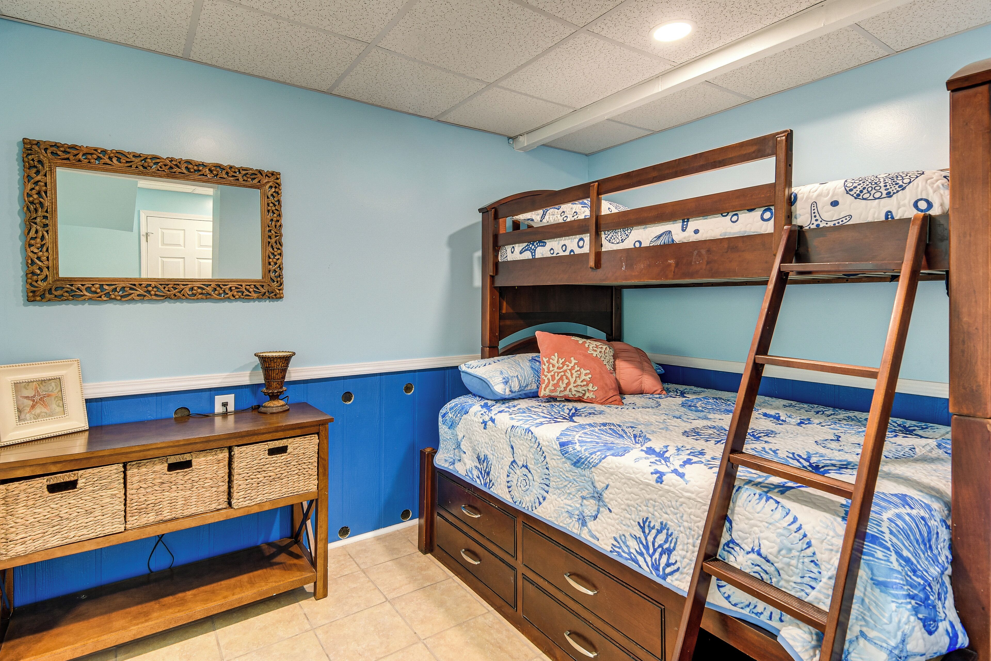 A bunk bed with a ladder, a dresser with baskets, and a mirror on the wall.