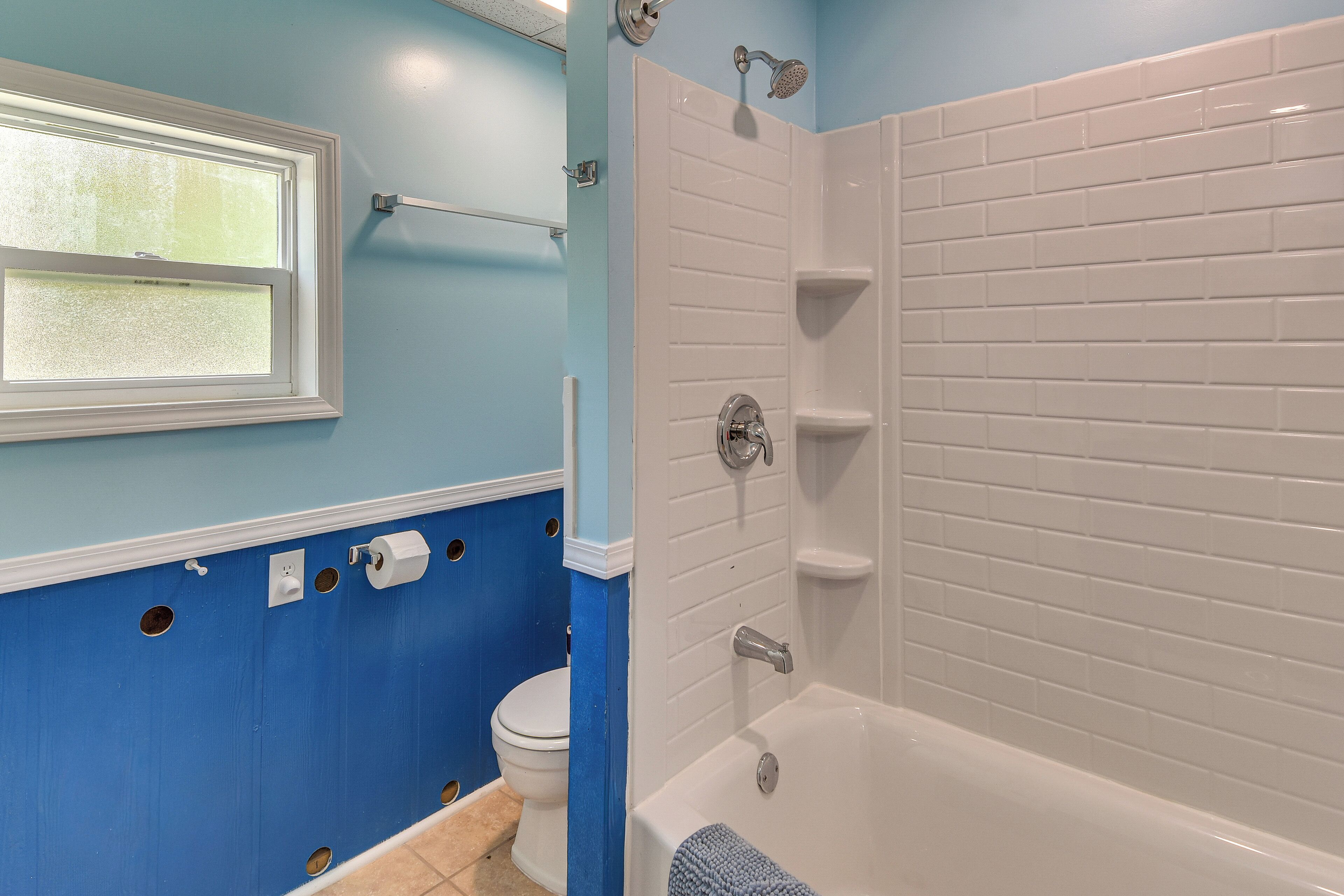 Une salle de bain avec une baignoire, des toilettes, une fenêtre et un porte-serviettes.