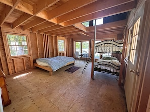 L'intérieur d'un chalet en bois, avec un lit, des lits superposés et de grandes fenêtres.