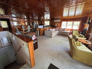 A wooden cabin interior with a kitchen, dining area, and living room furnished with a sofa and armchairs. - Tranquil Lakeside 2-Bedroom Cottage w/ Optional Bunkhouse (Eastbrook)