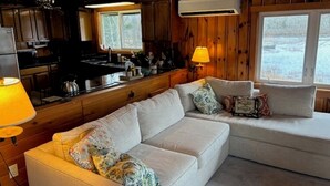 Un intérieur de chalet chaleureux, avec un revêtement mural en bois, un canapé, une table à manger et un coin cuisine.