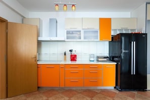 A kitchen with orange cabinets, a black refrigerator, and a wooden door.