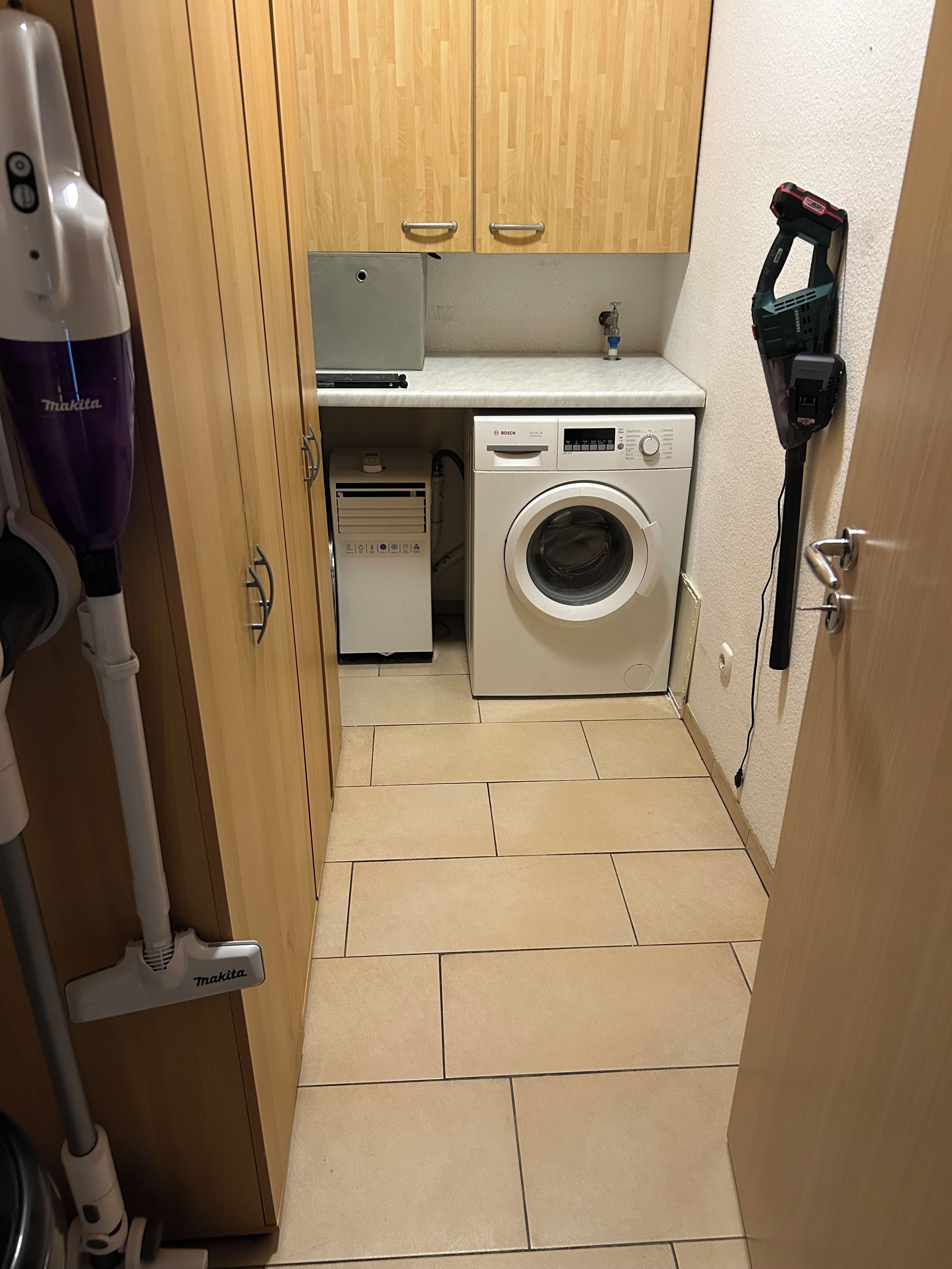 A compact laundry area with a Bosch washing machine, a Makita vacuum cleaner, and a power tool on a white countertop.