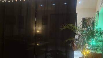 A room with a black curtain, a wooden side table, a potted plant, and a tiled floor.