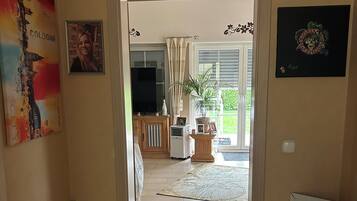 A doorway leading to a living room with a television, a potted plant, and a framed picture on the wall.