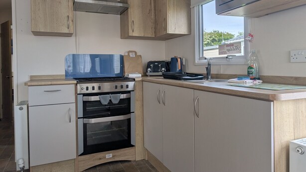A compact kitchen with a stove, oven, microwave, and wooden cabinets. - Coastal Comfort – Relaxing 3-Bed Holiday Home at Marlie Holiday Park (New Romney)