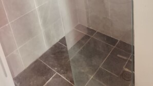 Laatoitettu suihkutila, jossa on lasiovi.