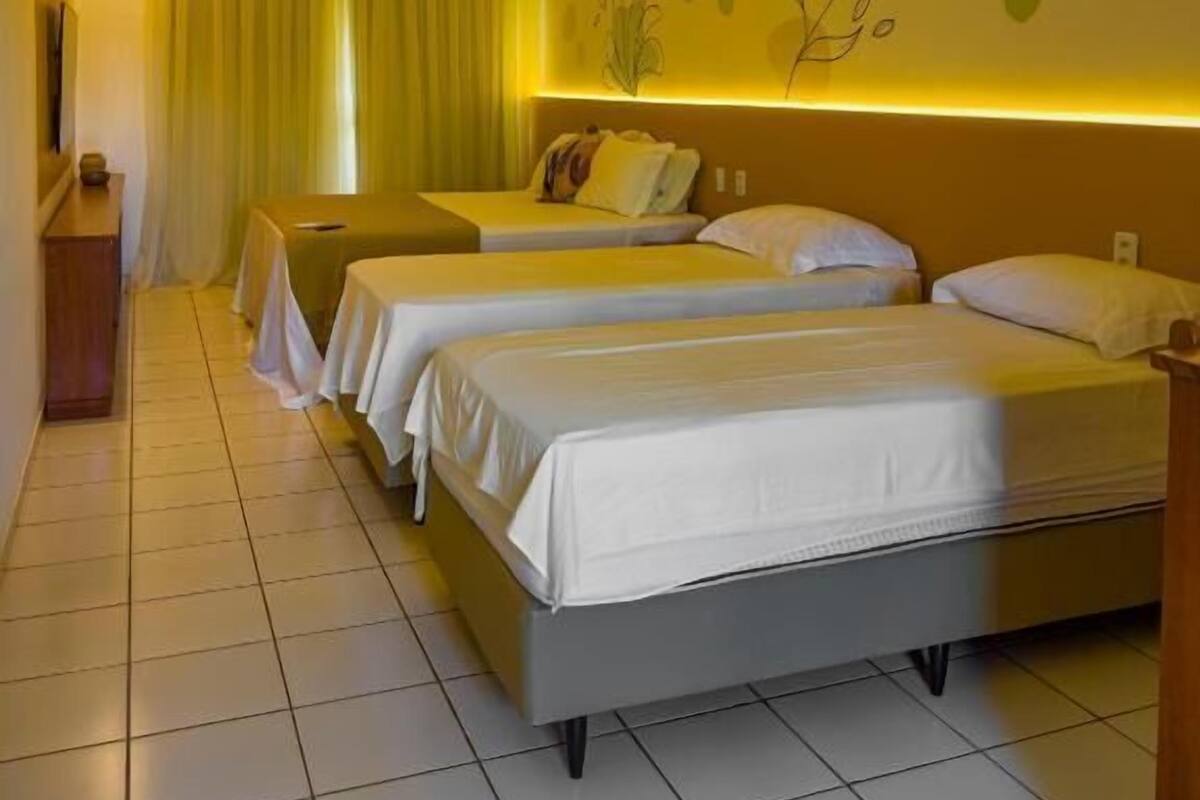 A hotel room with two beds, a bedside table, a wall with floral decorations, and a curtain.