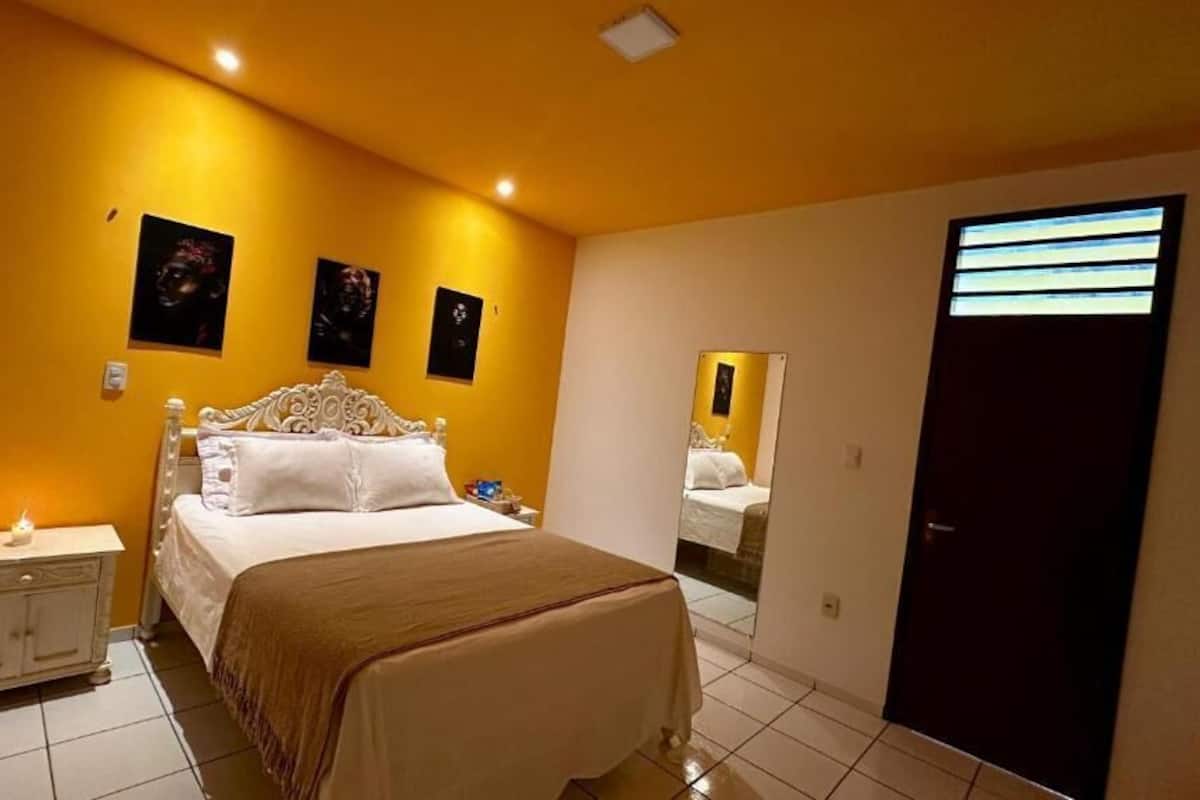 A bedroom with a bed, bedside table, and a mirror.