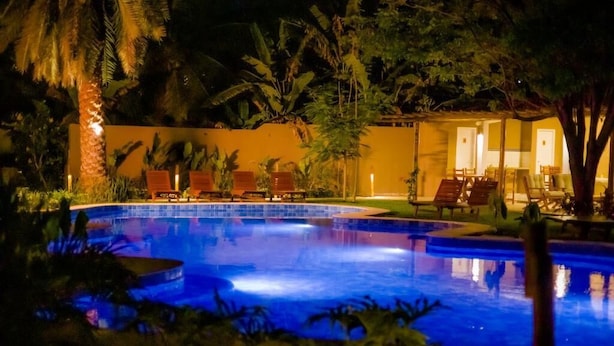 A swimming pool surrounded by palm trees and lounge chairs at night. - Villa jaguar (Fortim)
