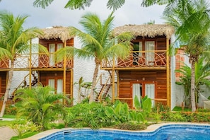 A resort with wooden cabins, a pool, and tropical vegetation.