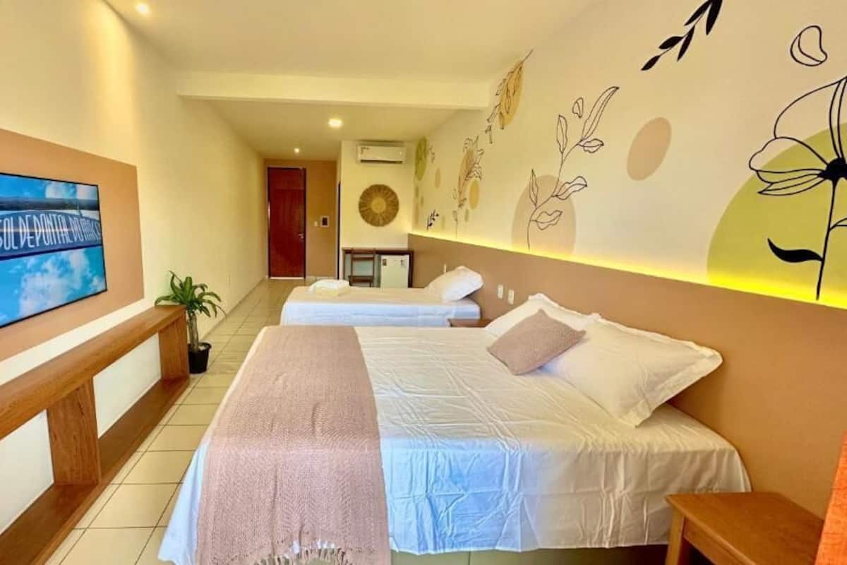 A hotel room with two beds, a TV, a desk, and a wall with a floral design.