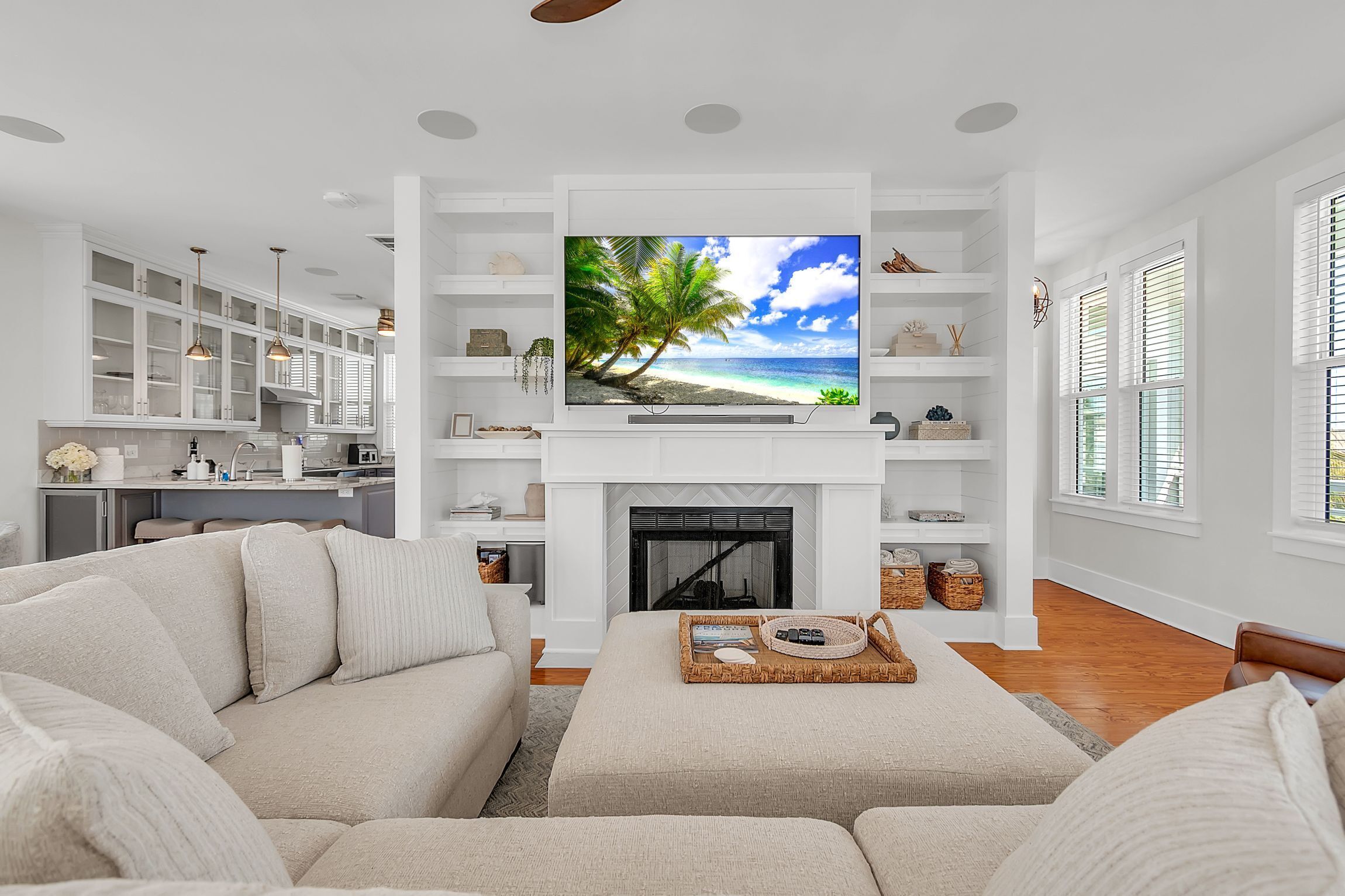 A living room with a TV, white furniture, a fireplace, and a kitchen in the background.