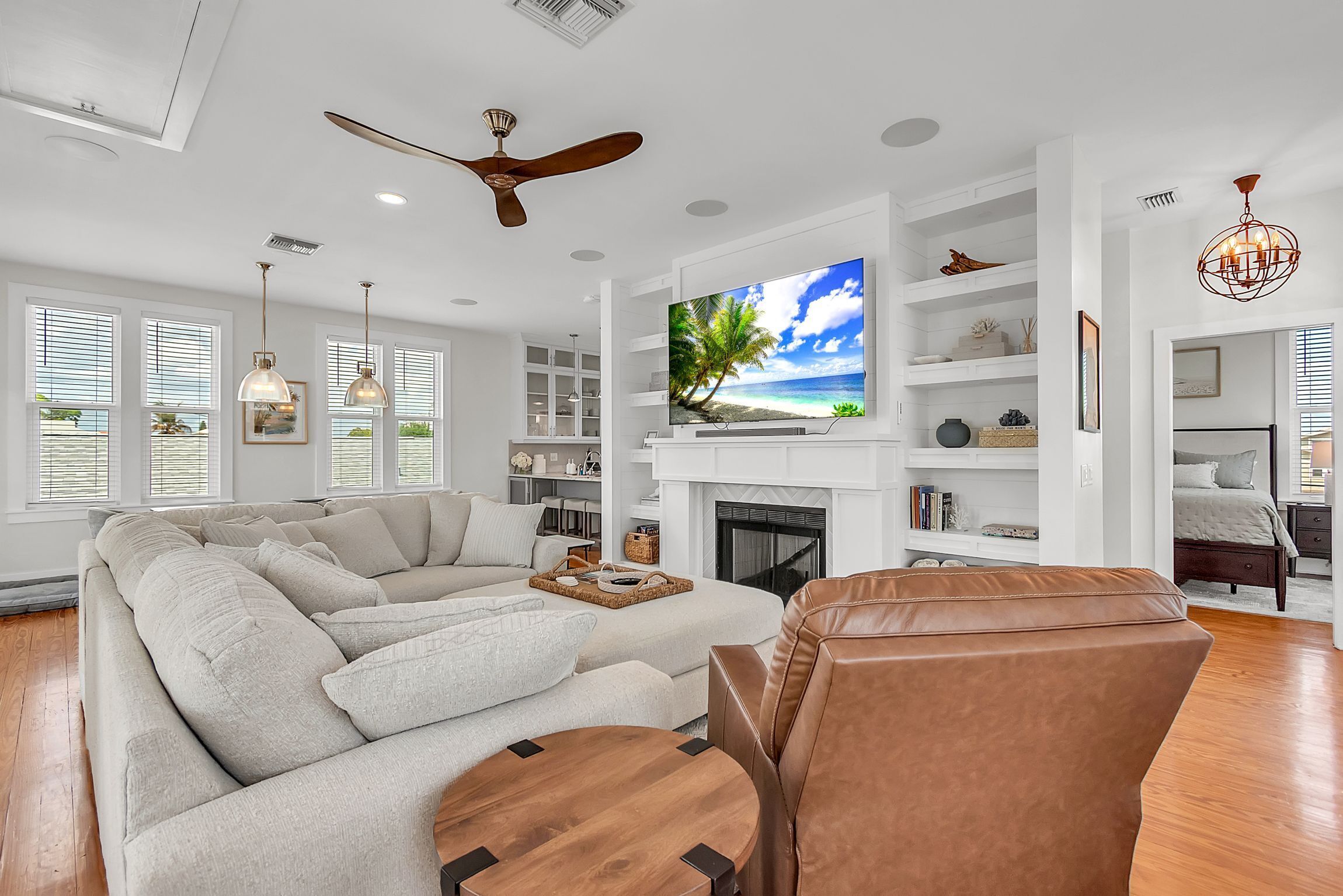 A modern living room with a large flat-screen TV, a fireplace, and a ceiling fan.