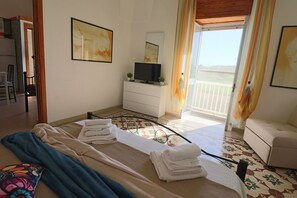 Una camera d'albergo con un letto, una TV, una cassettiera e un balcone con tende.