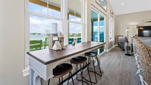 A kitchen with a long counter, bar stools, and a view of the outdoors. - Luxury Lagoon Front House w/ Elevator | Fire Pit | Boat Parking | Sleeps 10 (Gulf Shores)