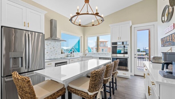 A modern kitchen with a central island, stainless steel appliances, and a view of buildings outside. - Luxury Lagoon Front House w/ Elevator | Fire Pit | Boat Parking | Sleeps 10 (Gulf Shores)