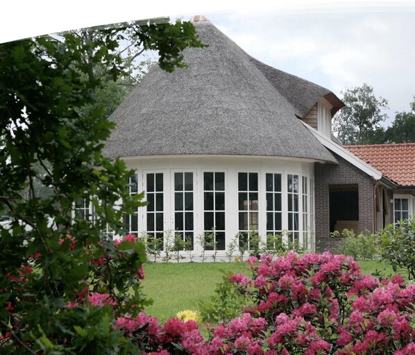 A house with a grey roof, a white windowed porch, and pink flowers in the foreground.