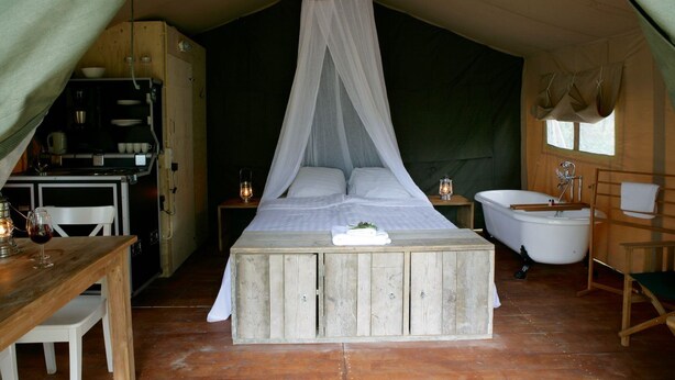Alojamiento tipo tienda con una cama, una mesa con un vaso, una lámpara, un lavabo y una silla.