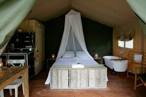 Ein Zelt mit Bett, Tisch mit Glas, Lampe, Spüle und Stuhl.