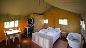 Una habitación con carpa, una cama, una mesa, una silla, un lavamanos y una estufa.