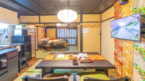 A traditional Japanese room with tatami flooring, a low table with a tablecloth, a bed with a futon, a television, and a sliding door. - 1 min. from Higashiyama Subway Station, 6 min. from Sanjo Station, 1 min. walk to Gion, 120 year old Kyomachiya, walking distance to Nishiki Market and Yasaka Shrine. (京都市左京区)
