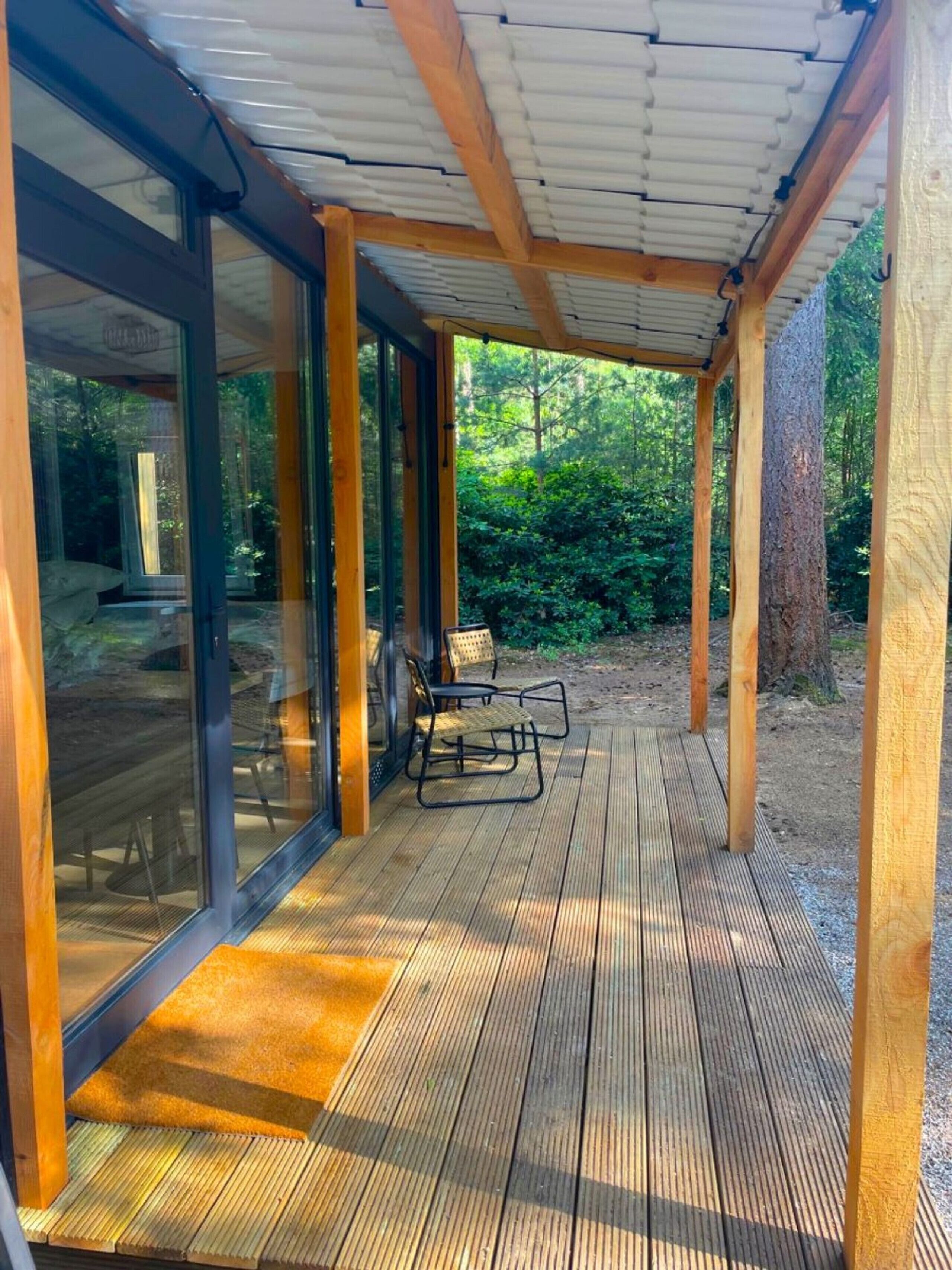 A covered wooden deck with glass doors leading to an outdoor seating area.