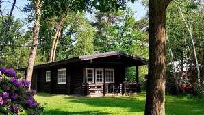 Une cabane en rondins dotée d’un porche, entourée d’une végétation luxuriante et d’arbres.