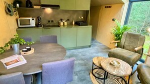 A compact kitchen with a microwave, kettle, and cabinets. There is a dining area with a table and chairs, and a view of greenery outside. - Outdoors Holten - Diamond Suite with Jacuzzi (Holten)