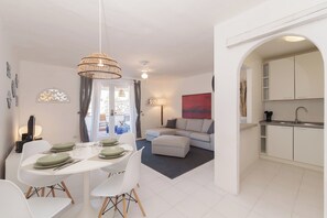 Una sala moderna con comedor, un sofá y una cocina con armarios blancos.