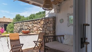 Una veranda esterna con pareti in pietra, arredi in legno e una lampada a sospensione.