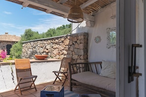 An outdoor patio with stone walls, wooden furniture, and a hanging light fixture. - VivimiHome-Porto Rotondo Dream Terrace (Porto Rotondo)