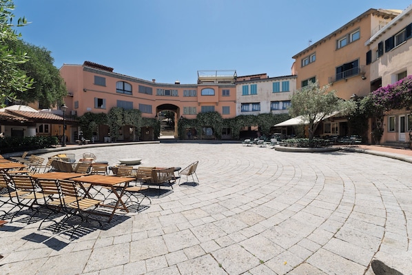 A courtyard with outdoor seating, a central archway, and multi-story buildings with balconies. - VivimiHome-Porto Rotondo Dream Terrace (Porto Rotondo)